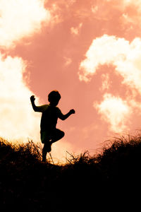 Silhouette boy standing on field against sky during sunset