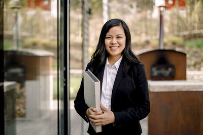 Portrait of confident female real estate agent standing outside house