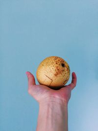 Close-up of hand holding pear against blue background