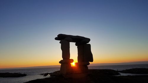 Silhouette rock on beach against clear sky during sunset