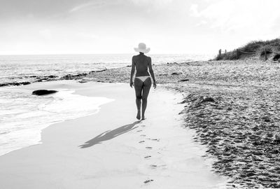 Rear view of sensuous woman wearing bikini while walking on sand at beach