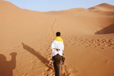 Rear view of man with camel walking on sand dune in desert