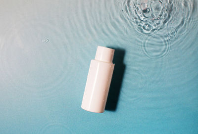 White cosmetic bottle in a blue pool with water and waves. spa skin care.