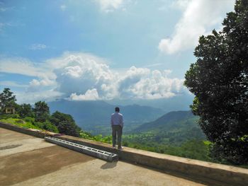 Rear view of man standing on mountain against sky