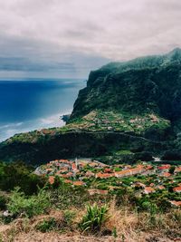 Idyllic view of sea by cliff against cloudy sky