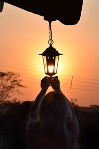 Silhouette woman igniting lantern against orange sky