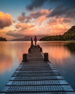 Rear view of people on pier over lake against sky during sunset