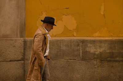 Adult man in hat and coat walking in front of yellow wall on street. madrid, spain