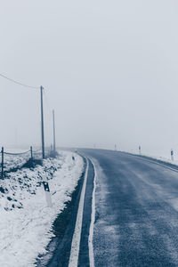Empty road leading towards snow covered landscape against sky