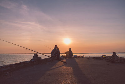 Men fishing on pier against sky during sunset