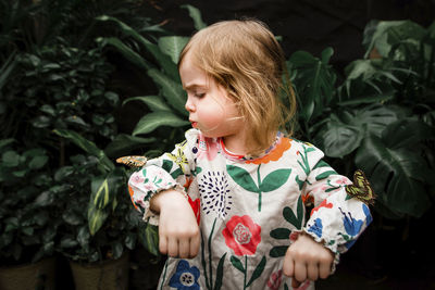Cute baby girl blowing butterfly on her hand against plants