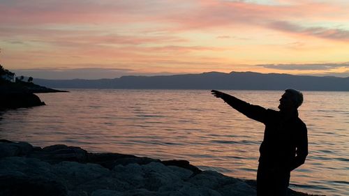 Silhouette man standing by lake during sunset