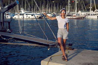 Woman in a white t-shirt and striped shorts standing on the pier next to the yacht