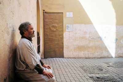 Side view of man sitting against wall