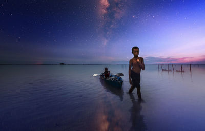 Full length portrait of boy pulling boat with friend at beach against sky