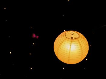 Low angle view of illuminated light bulb hanging at night