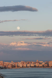 Sea by buildings against sky at sunset