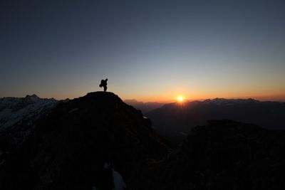 Silhouette man standing on rock against sky during sunset