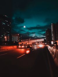 Illuminated street amidst buildings against sky at night