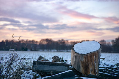 Wooden posts on snow covered land against sky during sunset