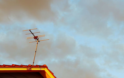 Low angle view of television aerial on house roof against sky