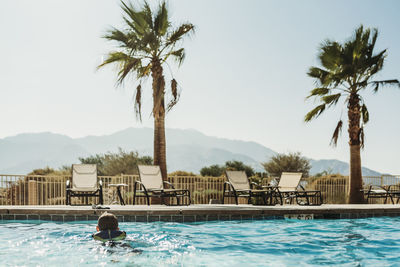 Rear view of man swimming in pool against sky