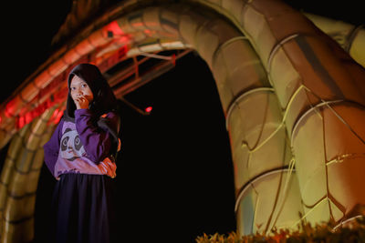 Young woman standing against illuminated wall