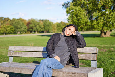 Portrait of young woman sitting on bench against trees