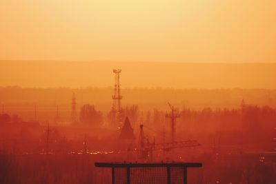 Silhouette factory against sky during sunset