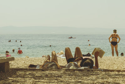 People relaxing at beach against clear sky