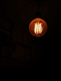 Low angle view of illuminated light bulb hanging at night