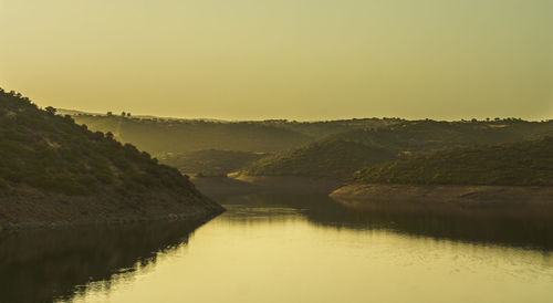 Scenic view of river and mountains against sky at sunset