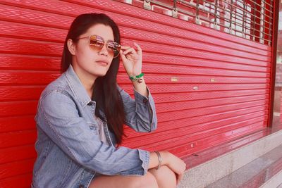 Portrait of beautiful young woman wearing sunglasses against wall