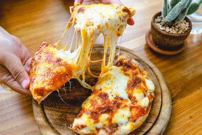 High angle view of hand holding pizza on table