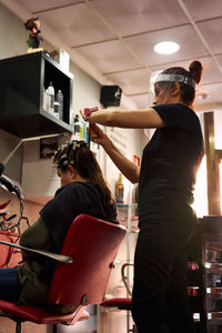 Hairdresser combs a client with a face shield in her salon