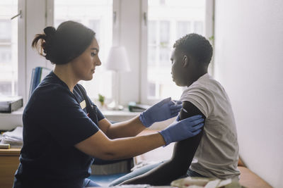 Side view of female nurse giving vaccine on patient's arm at hospital