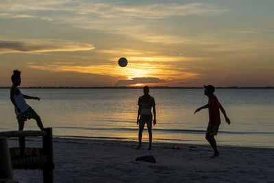 Silhouette people playing with ball on beach against sky during sunset