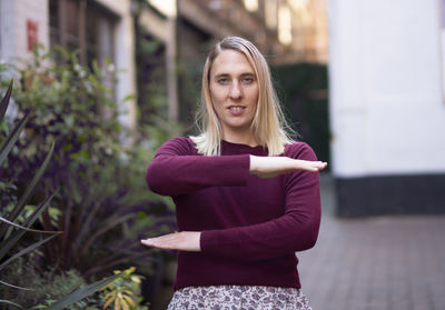 Portrait of smiling young woman gesturing while standing outdoors