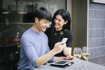 Smiling young woman using mobile phone while sitting on table