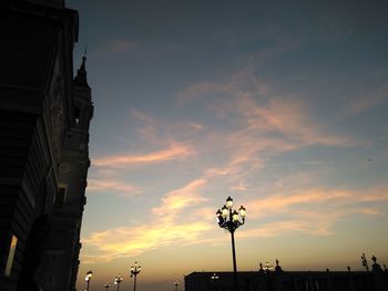 Low angle view of building and street lights against cloudy sky