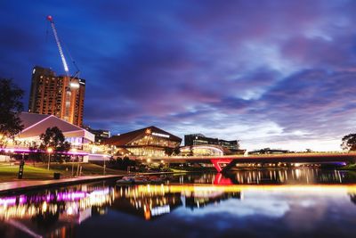 Illuminated buildings by river against sky at night
