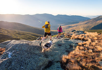 Man and woman trail running with dog in mountains at sunrise