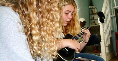 Young woman sitting by girl playing guitar at home