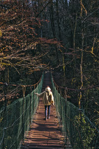 Rear view of woman walking on footbridge in forest