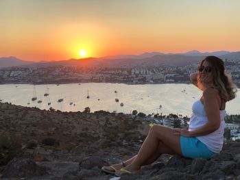 Side view of young woman sitting on rock during sunset