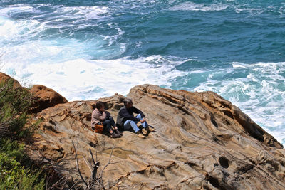 High angle view of people sitting on rock by sea