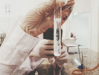 Cropped scientist doing chemical experiment while colleague photographing in laboratory