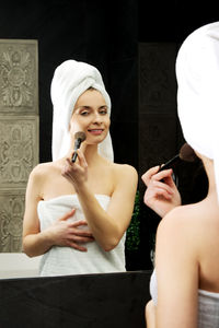 Portrait of young woman holding camera while standing in bathroom