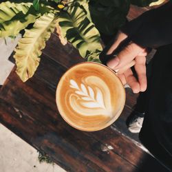 Cropped hand of person holding coffee over table at home