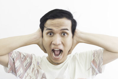Portrait of frustrated man covering ears against white background